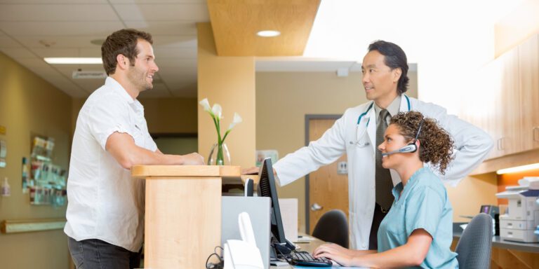 Patient With Doctor And Nurse At Reception Desk